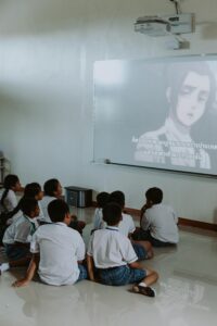 Group of school children watching anime on a projector screen indoors.