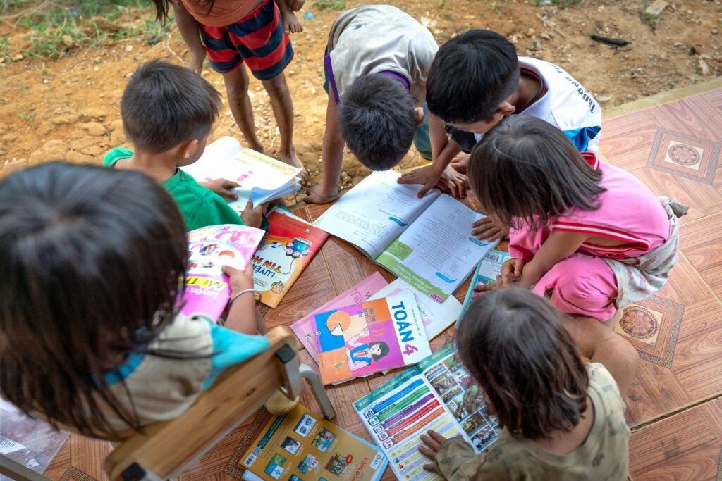 Children gathered outdoors, actively engaged in reading and learning from books.